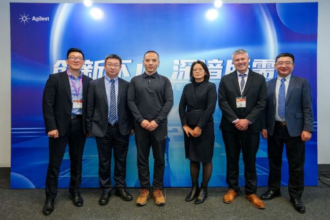 A group of people standing in front of a blue signDescription automatically generated